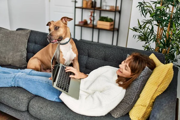 若いですCaucasian女性使用ラップトップ上に横たわるとともに犬とともに自宅 — ストック写真