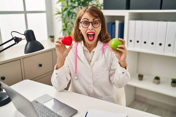 年轻的女医生拿着红绿相间的苹果庆祝着疯狂的成功 睁大了眼睛兴奋地尖叫着 — 图库照片