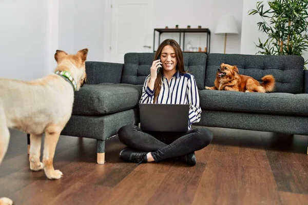 若いヒスパニック系の女性がラップトップを使用して 自宅で犬と床に座ってスマートフォンで話しています — ストック写真