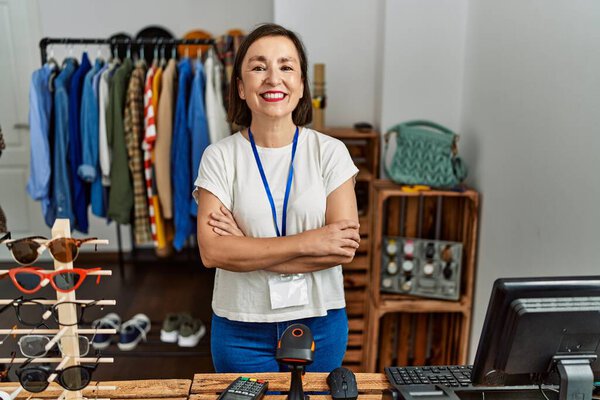 Beautiful middle age hispanic woman working as manager at retail boutique happy face smiling with crossed arms looking at the camera. positive person. 