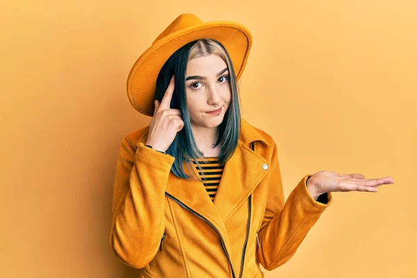 黄色の帽子と革のジャケットを身に着けている若い現代の少女は コピースペースと額に指を指すことを示す開いてヤシの木に混乱し 悩まされました 考えてみてください — ストック写真
