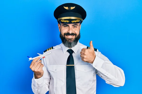 Joven Hombre Hispano Vistiendo Uniforme Piloto Sosteniendo Juguete Plano Sonriendo —  Fotos de Stock