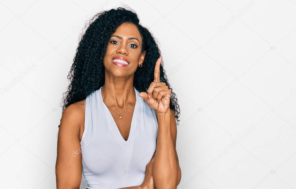 Middle age african american woman wearing casual style with sleeveless shirt with a big smile on face, pointing with hand and finger to the side looking at the camera. 