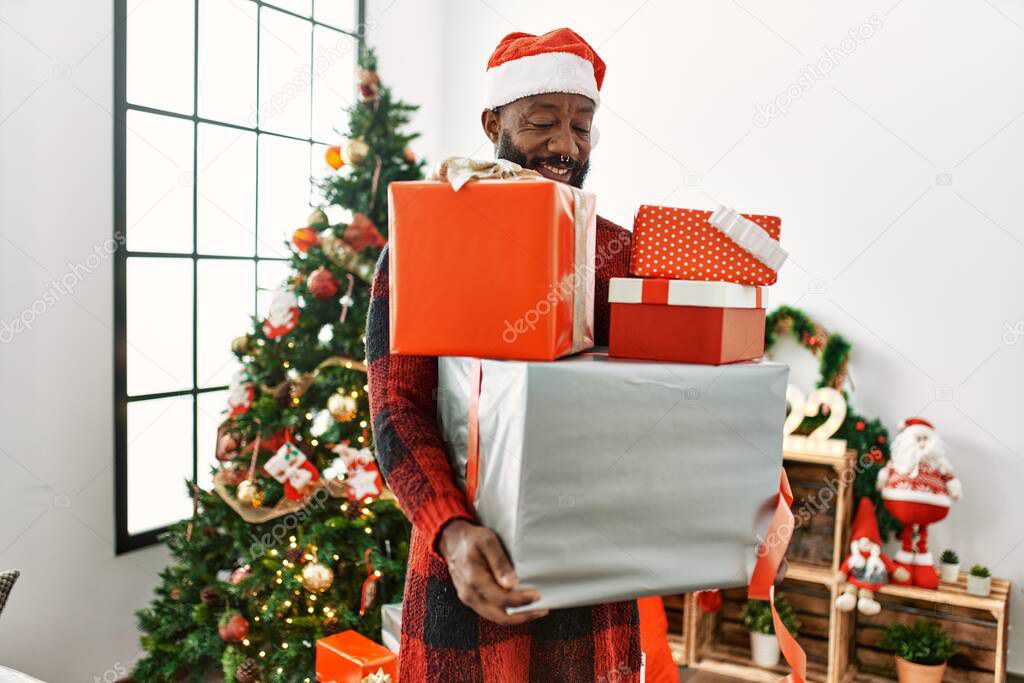 Young african american man holding gifts standing by christmas tree at home