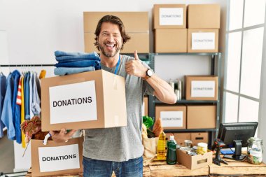 Gönüllü standında bağış kutusunu tutan yakışıklı orta yaşlı bir adam elleriyle mutlu bir jest yapıyor. Kameraya bakıp başarıyı gösteren ifade. 