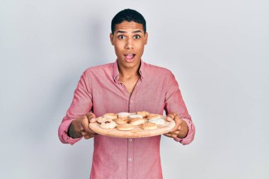 Genç Afrikalı Amerikalı çocuk elinde pasta tepsisiyle şaşırmış ve şaşırmış bir ifadeyle korku ve heyecanlı bir yüz ifadesiyle. 