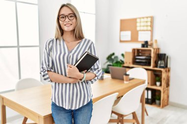 Ofiste kitap tutan genç Çinli kadın gülümsüyor.