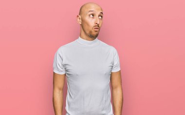 Sakallı, sıradan beyaz tişörtlü, kel bir adam. Gülümsüyor, yan tarafa bakıyor ve düşünüyor.. 