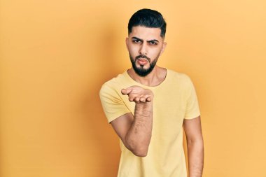 Yakışıklı, sakallı, sıradan sarı tişörtlü bir adam kameraya bakıyor ve havada bir öpücük savuruyor. Güzel ve seksi. aşk ifadesi. 