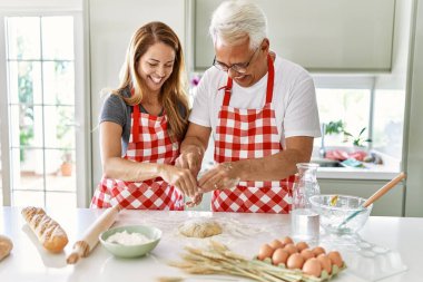 Orta yaşlı İspanyol çift gülümseyerek mutfakta mutlu ekmek pişiriyor..