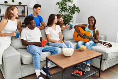 Mutlu gülümseyen ve evde klasik gitar çalan bir grup genç arkadaş..