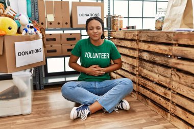 Bağışlarda gönüllü tişört giyen Afro-Amerikalı genç bir kadın mide bulantısı ve acı verici bir hastalıktan dolayı el üstünde duruyor. Ağrı kavramı. 