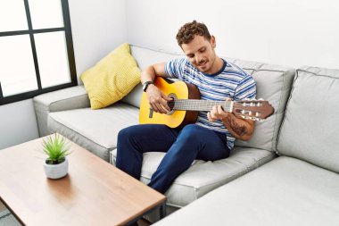 Evde klasik gitar çalarak kendinden emin gülümseyen İspanyol genç adam.