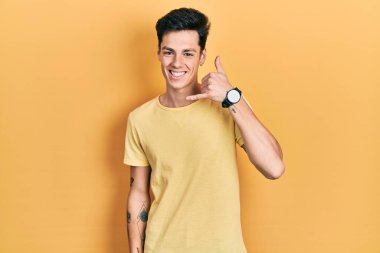 Sarı tişört giyen genç İspanyol adam gülümsüyor telefonla el ve parmaklarıyla jest yapıyor telefonda konuşuyor gibi. iletişim kavramları. 