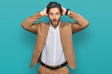İş kıyafetleri giymiş genç İspanyol bir adam çılgın ve elleri başında korkmuş, ağzı açık şoktan korkmuş ve şaşırmış. 