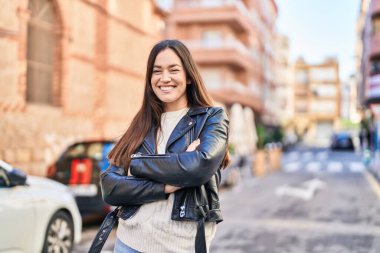 Kendine güvenen genç bir kadın caddede kollarını kavuşturmuş duruyor.