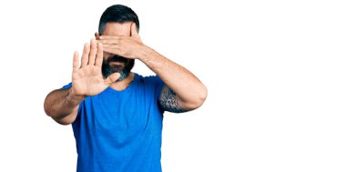 Sakallı, sıradan tişörtlü, gözlüklü, elleriyle gözlerini kapatan üzgün ve korku ifadeli İspanyol bir adam. utangaç ve olumsuz kavram. 