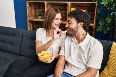 Erkek ve kadın, evde patates cipsi yerken kendinden emin bir şekilde gülümsüyor.