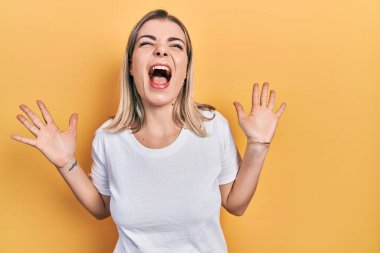Beyaz rahat tişörtler giyen güzel beyaz kadın başarı için deli ve çılgınlığı kutluyor kollarını kaldırmış ve gözlerini kapatmış heyecanla bağırıyor. Kazanan konsept 