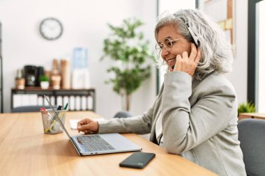 Orta yaşlı, gri saçlı çağrı merkezi ajanı kadın ofiste çalışırken mutlu bir şekilde gülümsüyor..