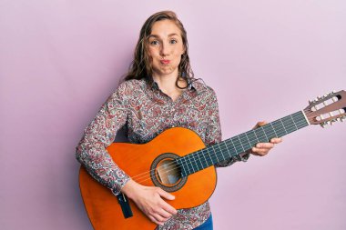 Sarışın, klasik gitar çalan, komik yüzlü genç bir kadın. Ağzı havayla şişer, havayı yakalar.. 