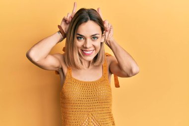 Genç, beyaz, sarı tişört giyen, komik ve deli pozu veren, parmakları tavşan kulaklı, neşeli gülümseyen sarışın kadın. 
