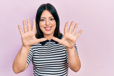 Genç İspanyol kadın gündelik giysiler giyer ve parmaklarını on numara ile gösterir ve gösterirken kendinden emin ve mutlu gülümser.. 