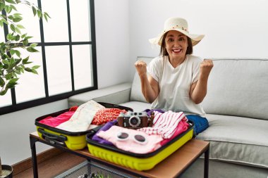 Güzel, orta yaşlı İspanyol bir kadın, yaz kıyafetlerini bavula koyup kollarını kaldırıp, gözleri açık bir şekilde başarıya ulaşmasını kutluyor. Kazanan konsept. 