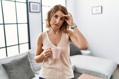 Orta yaşlı bir kadın evde kahve içiyor. Alnındaki sorun yüzünden endişeli ve stresli. Kriz için endişeli. 