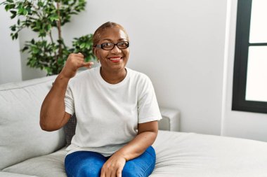 Olgun İspanyol kadın evinde koltukta oturmuş gülümsüyor telefonla el ve parmak hareketleri yapıyor telefonda konuşuyor gibi. iletişim kavramları. 