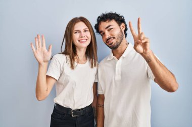 Genç çift gündelik giysiler giyip yedi numaralı parmaklarını gösterip işaret ederken mutlu ve kendinden emin bir şekilde gülümsüyor.. 
