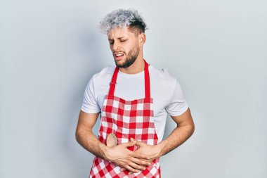 Modern boyalı saçlı, elleri karnında önlük giyen genç İspanyol bir adam. Çünkü mide bulantısı, acı verici bir hastalık kendini iyi hissetmiyor. Ağrı kavramı. 