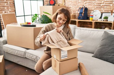 Yeni evinde kendine gülen beyaz bir kadın boks paketini açıyor.
