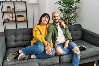 Genç İspanyol çift mutlu bir şekilde gülümsüyor ve evdeki kanepede oturup sarılıyorlar..