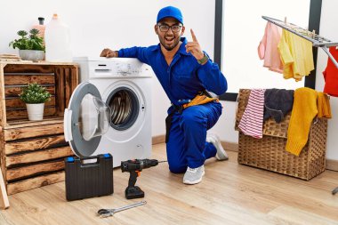 Çamaşır makinesi üzerinde çalışan genç Hintli teknisyen başarılı bir fikri işaret ediyor. Heyecanlı ve mutlu. Bir numara.. 