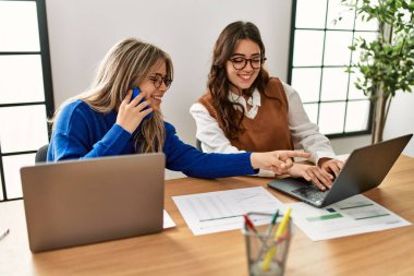 İki iş kadını akıllı telefonla konuşuyor ve ofiste dizüstü bilgisayar kullanıyor..