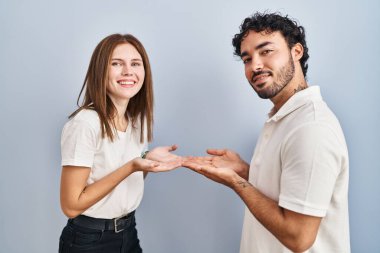 Gündelik giysiler giymiş genç bir çift ellerini yana uzatmış fotokopi alanını gösteren avuç içleri açık bir şekilde gülümseyerek mutlu bir gülümseme sergiliyorlar. 