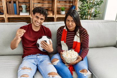 Evdeki kanepede oturan genç latin çift futbol maçını izliyor ve destekliyor..