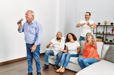 Bir grup orta yaşlı arkadaş evde mikrofon kullanarak şarkı söylüyor..