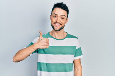 Gündelik kıyafetler giyen genç İspanyol adam elleriyle mutlu bir jest yapıyor. Kameraya bakıp başarıyı gösteren ifade. 