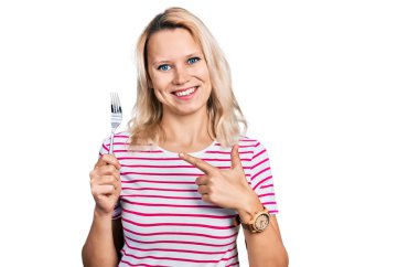 Bir gümüş çatal tutan genç beyaz kadın mutlu bir şekilde elini ve parmağını gösterdi. 