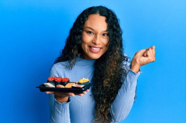 Genç Latin kadın bir tabak suşi gösteriyor. Gururla haykırıyor, zaferi kutluyor ve kollarını kaldırdığında çok heyecanlanıyor. 