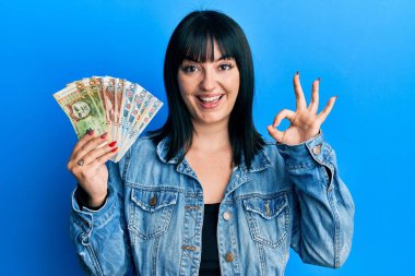 Elinde Perulu sol banknotları tutan genç İspanyol kadın parmaklarıyla imza atıyor, gülümseyerek mükemmel bir sembol oluşturuyor. 