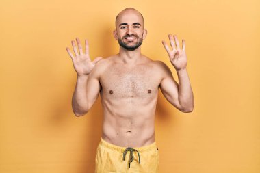 Mayo giyen genç kel adam dokuz numarayı gösterip işaret ederken kendinden emin ve mutlu bir şekilde gülümsüyor.. 