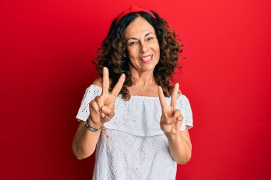 Orta yaşlı İspanyol kadın, sıradan kıyafetler giyip kameraya bakıp zafer işareti yapıyor. İki numara.. 