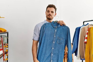 Genç İspanyol müşteri gülümsüyor. Giysi mağazasında tişörtlü bir askı tutuyor..