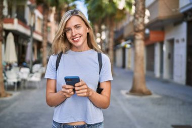 Sokakta akıllı telefon kullanan, kendine güvenen genç sarışın kadın.