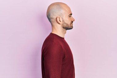 Sıradan kıyafetler giyen genç kel bir adam, rahat bir görünüm takınıyor, kendine güvenen bir gülümsemeyle doğal bir yüzle poz veriyor.. 