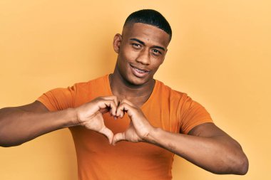 Gündelik turuncu tişört giyen genç siyahi bir adam. Sevgiyle gülümsüyor. Elleriyle kalp sembolü ve şekli gösteriyor. romantik kavram. 