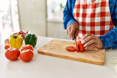 Kıdemli adam mutfakta domates kesiyor.